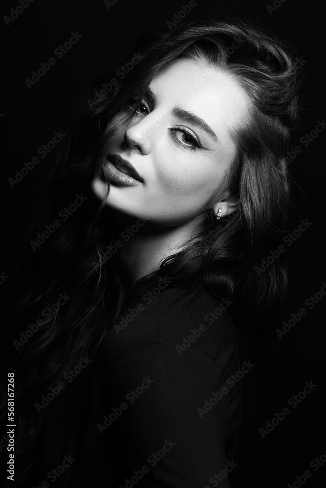 Make-up and fashion concept. Brunette woman with long wavy hair sensual studio portrait. Model wearing blouse and looking at camera with seductive look. Dark studio background. Black and white image
