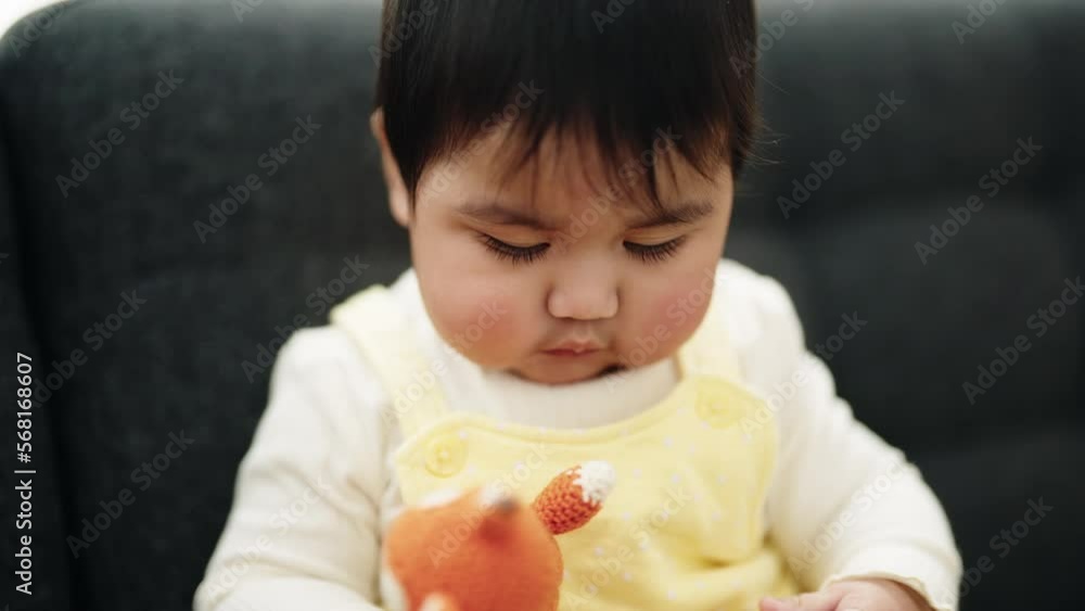 Adorable hispanic baby holding toy sitting on sofa at home Adorable hispanic baby holding toy sitting on sofa at home