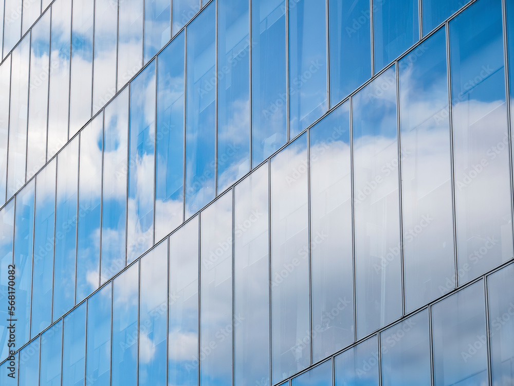 The sky with white clouds reflecting in the glass windows of a modern office building.