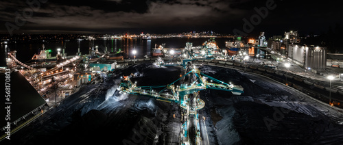 Rotary shovel at coal pile, bulk shipping terminal, silos, grain elevators, freight vessels, North Vancouver, BC.