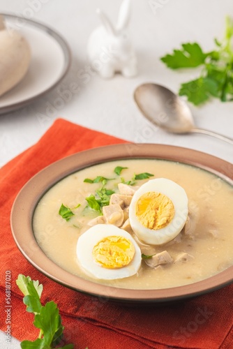 Polish Easter soup Zurek with white sausages and a boiled egg in a green ceramic bowl on a light concrete background. Traditional Polish Easter dishes.