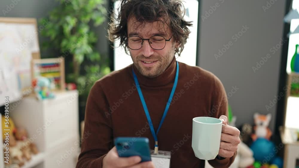 Young hispanic man preschool teacher using smartphone drinking coffee at kindergarten Young hispanic man preschool teacher using smartphone drinking coffee at kindergarten