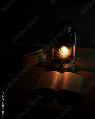 An ancient kerosene lamp, standing on the table, a book next to it, darkness around. Black background, light from a lamp