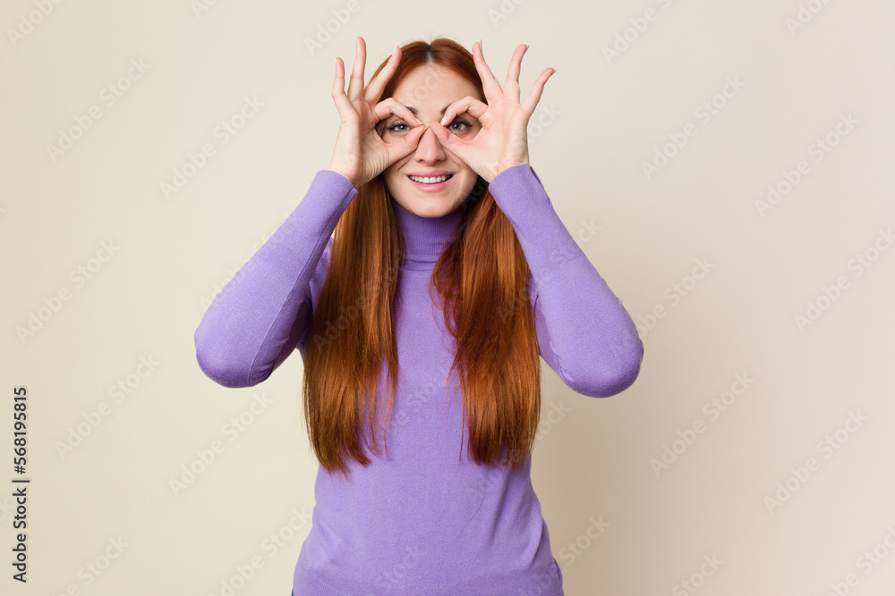 Young red hair woman isolated showing okay sign over eyes Young red hair woman isolated showing okay sign over eyes