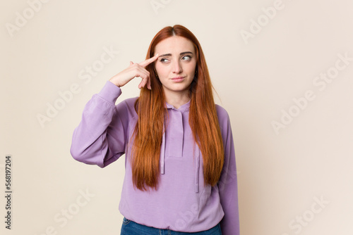 Young red hair woman isolated pointing temple with finger, thinking, focused on a task. © Asier