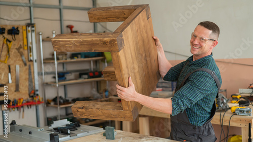 Male carpenter finishing work on wooden table in workshop. 