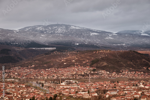 Sunlit cityscape and distant mountains in the shadow on a winter day with dark, moody sky © Nikola