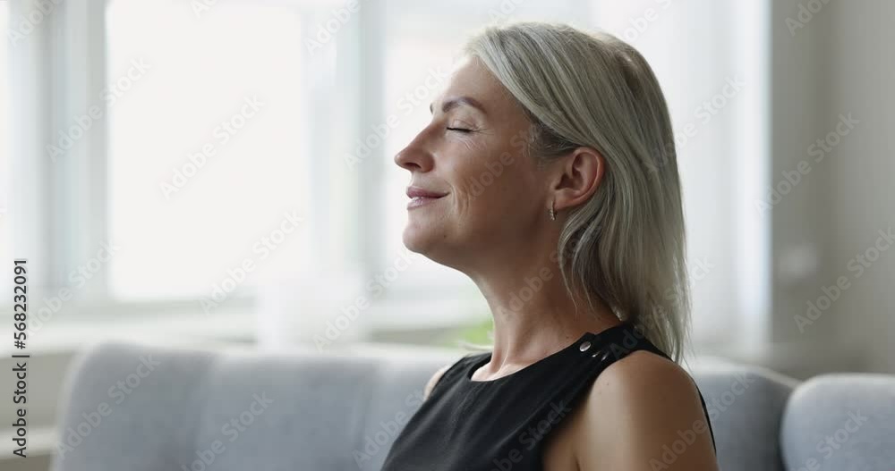 Serene mature woman taking deep breath, relish pleasant fragrance, breathe fresh air, meditate with eyes closed sit on sofa, close up. Enjoy moment of peace, do mental relaxation practice, no stress Serene mature woman taking deep breath, relish pleasant fragrance, breathe fresh air, meditate with eyes closed sit on sofa, close up. Enjoy moment of peace, do mental relaxation practice, no stress