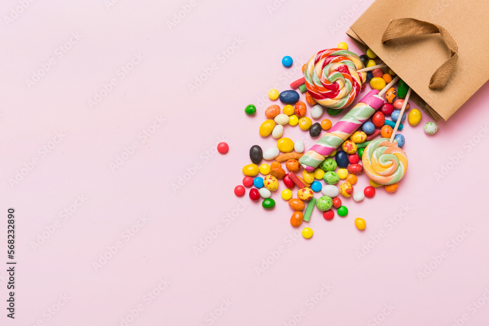shopping paper gift bag in corner full of assorted traditional candies falling out on colored background with copy space. Happy Holidays sale concept shopping paper gift bag in corner full of assorted traditional candies falling out on colored background with copy space. Happy Holidays sale concept