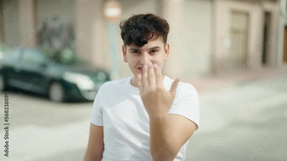 Non binary man smiling confident doing coming gesture with hand at street Non binary man smiling confident doing coming gesture with hand at street