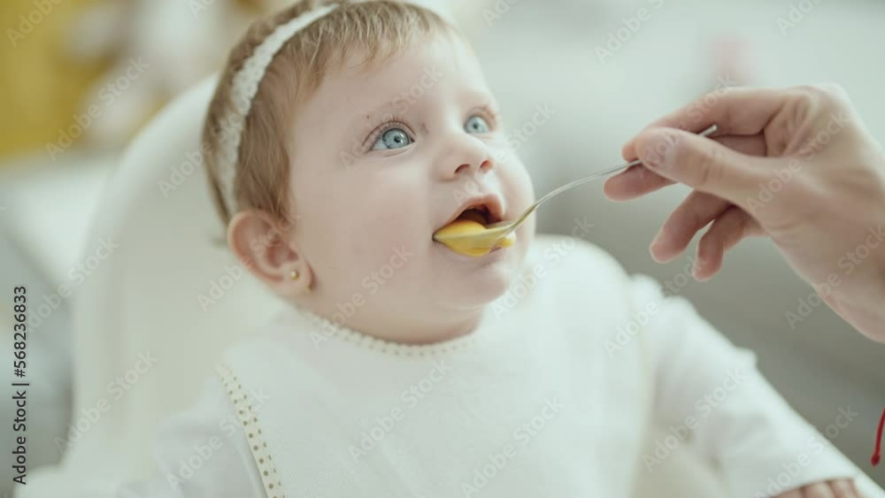 Adorable blonde baby sitting on highchair eating at home Adorable blonde baby sitting on highchair eating at home