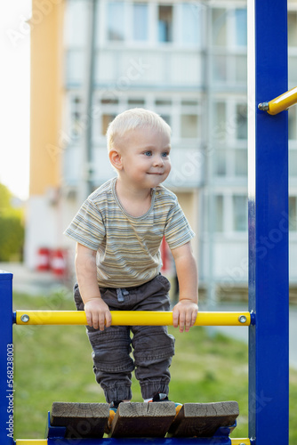 Little boy climbs on playground. Cute smiling kid playing outdoors. Concept of kindergarten © Olha Tsiplyar