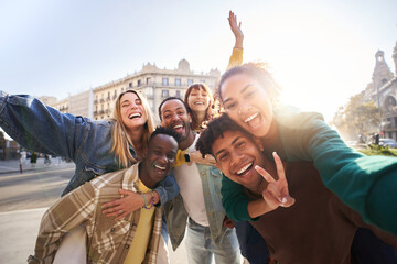 A group of cheerful students college friends having fun together as they travel through European cities. Happy community of diverse people. Selective focus on the smily couple taking the selfie.