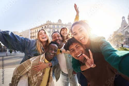 A group of cheerful students college friends having fun together as they travel through European cities. Happy community of diverse people. Selective focus on the smily couple taking the selfie.