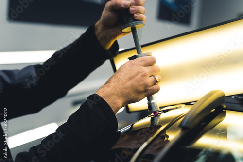 Photography Unrecognizable male mechanic removing dents from car body using bright lamp and specialistic equipment