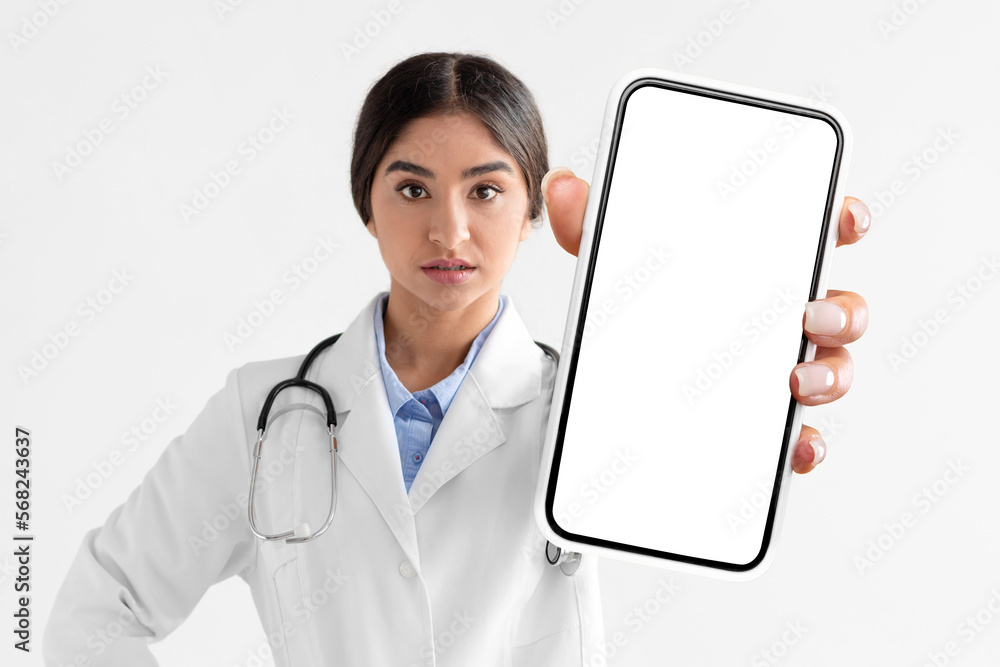 Mobile Mockup. Serious Indian Female Doctor Showing Big Blank Cellphone At Camera Mobile Mockup. Serious Indian Female Doctor Showing Big Blank Cellphone At Camera