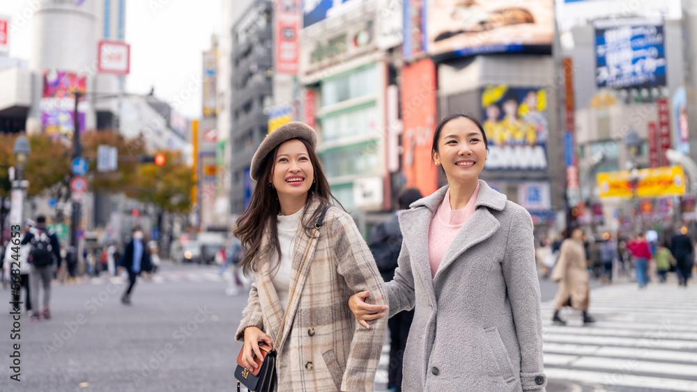 Asian woman friends crossing street crosswalk with crowd of people during shopping at Shibuya, Tokyo, Japan in autumn. Attractive girl enjoy and fun outdoor lifestyle travel city on holiday vacation.