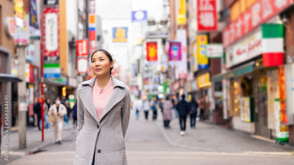 Asian woman looking modern building cityscape during travel at Shibuya district, Tokyo city, Japan. Attractive girl enjoy and fun outdoor lifestyle shopping in the city on autumn holiday vacation.