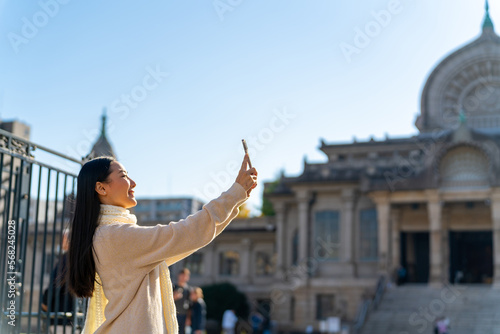 Young Asian woman using mobile phone taking picture while travel and shopping in the city in Tokyo, Japan. Attractive girl enjoy and fun outdoor lifestyle travel city street on autumn holiday vacation