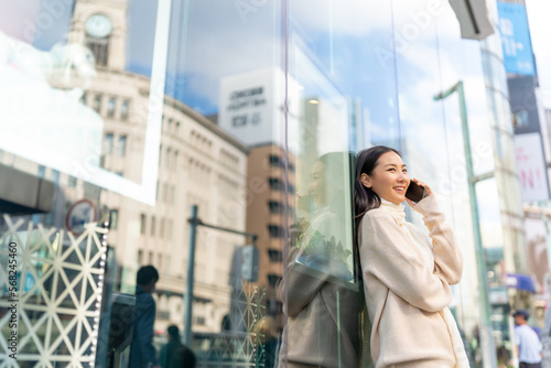Asian woman talking on mobile phone during shopping at Shibuya district, Tokyo city, Japan with crowd of people walking background. Attractive girl enjoy travel city street on autumn holiday vacation