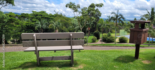 An isolated wooden park bench next to a walking path with trees, palm trees and tennis court. photo