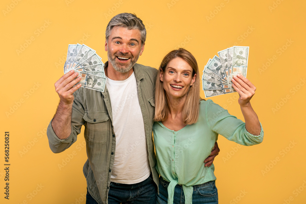 A lot of money, joy of victory. Happy middle aged caucasian couple holding many dollars, expressing emotions of success A lot of money, joy of victory. Happy middle aged caucasian couple holding many dollars, expressing emotions of success