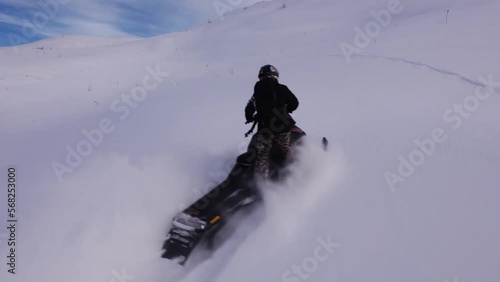 A man on a snowmobile roams the mountains 2023 filming from a drone