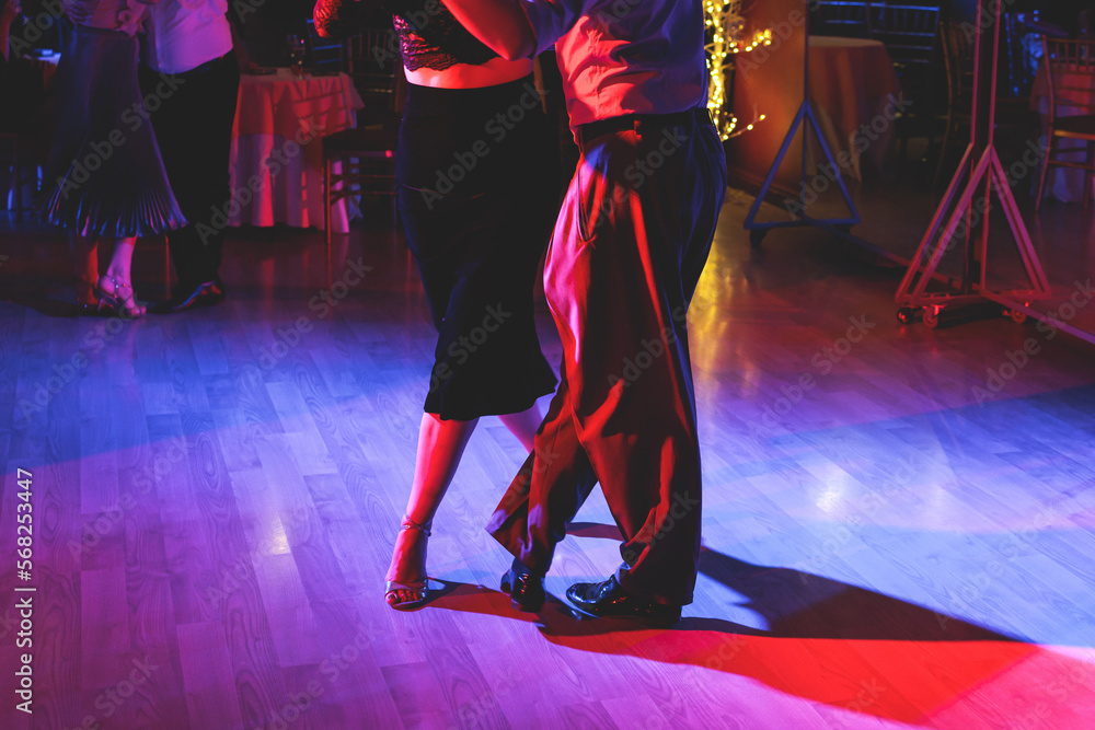 Fototapeta premium Couples dancing traditional latin argentinian dance milonga in the ballroom on a festival, tango studio, salsa, bachata and kizomba lesson in the red and purple lights, rehearsal in the dance class