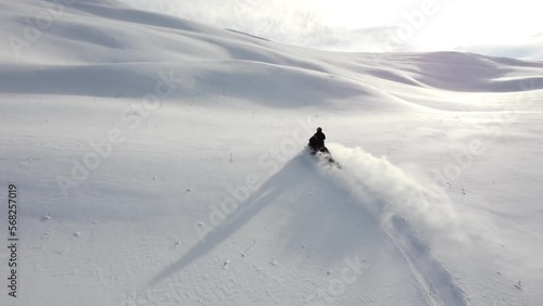 A man on a snowmobile roams the mountains 2023 filming from a drone