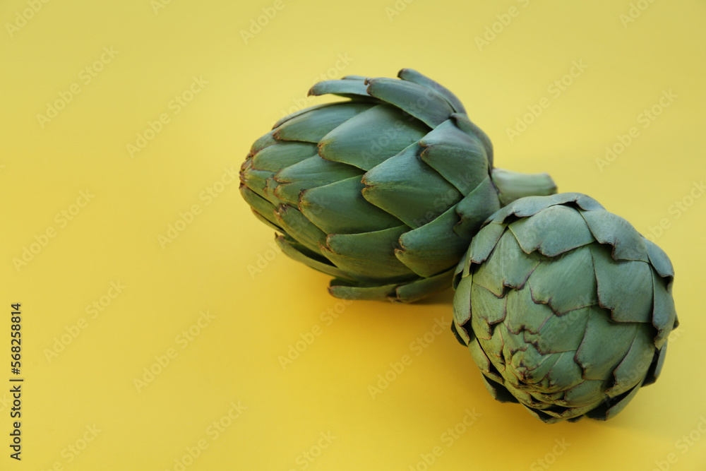 Fototapeta premium Whole fresh raw artichokes on yellow background, closeup. Space for text