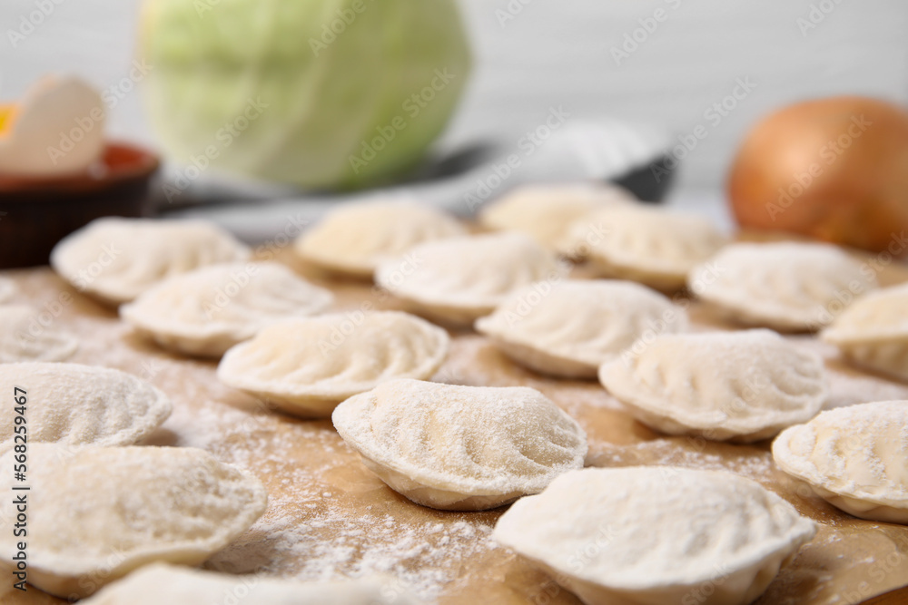 Raw dumplings (varenyky) with tasty filling and flour on parchment paper, closeup view Raw dumplings (varenyky) with tasty filling and flour on parchment paper, closeup view