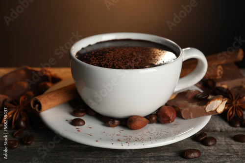 Cup of delicious hot chocolate, spices and coffee beans on wooden table