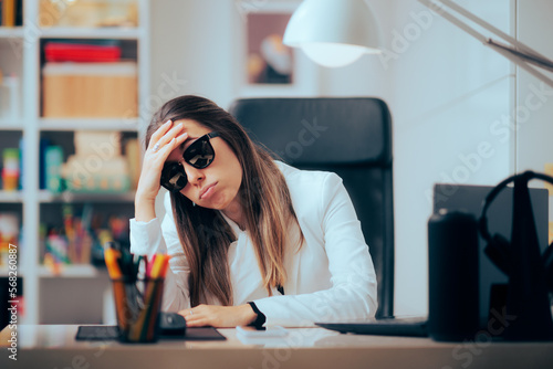 Tired Office Worker Wearing Sunglasses at the Office. Woman suffering from photosensitivity to indoor fluorescent light
 photo