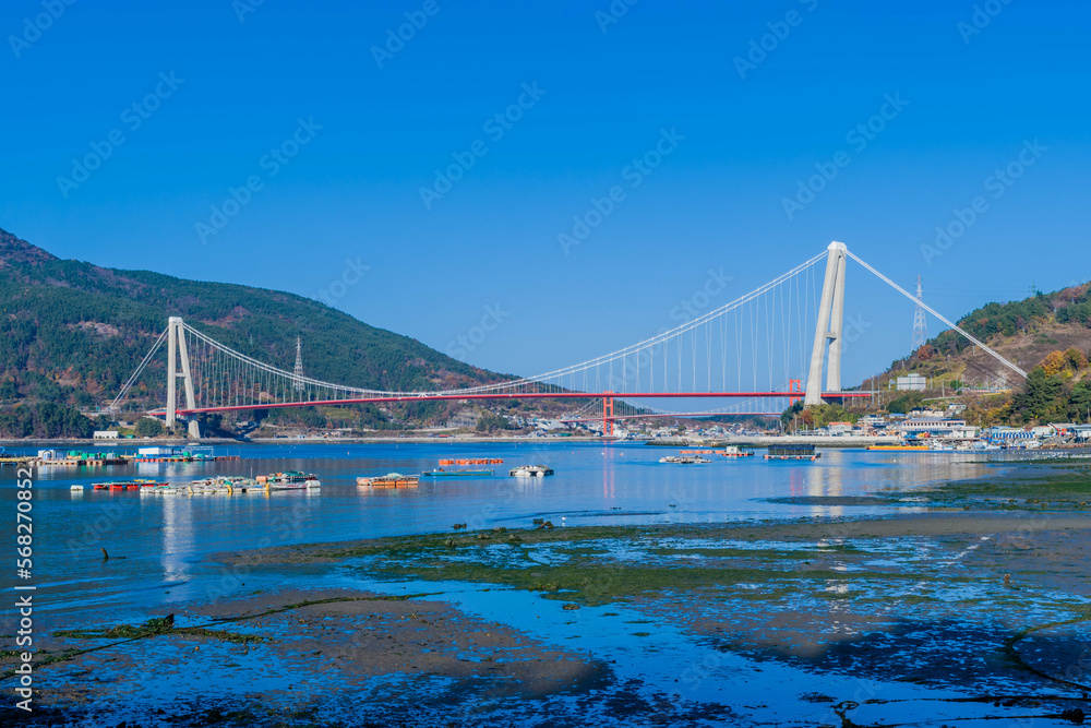 Seascape of ocean harbor at low tide with bridge in background.