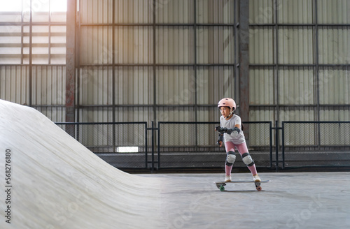 asian child skater or kid girl playing skateboard or ride surf skate up to wave ramp or wave bank to fun bottom turn in skate park by extreme sports surfing to wear helmet knee support for body safety