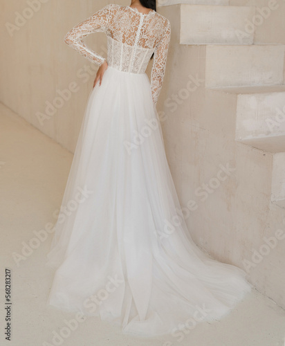 Back view of beautiful brunet bride in the white wedding dress. Gorgeous wedding dress with stylish elegance sleeves, decorated with lace. Wedding lacy corset with buttons