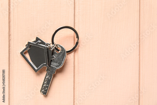 Key with house shape keychain on color wooden background