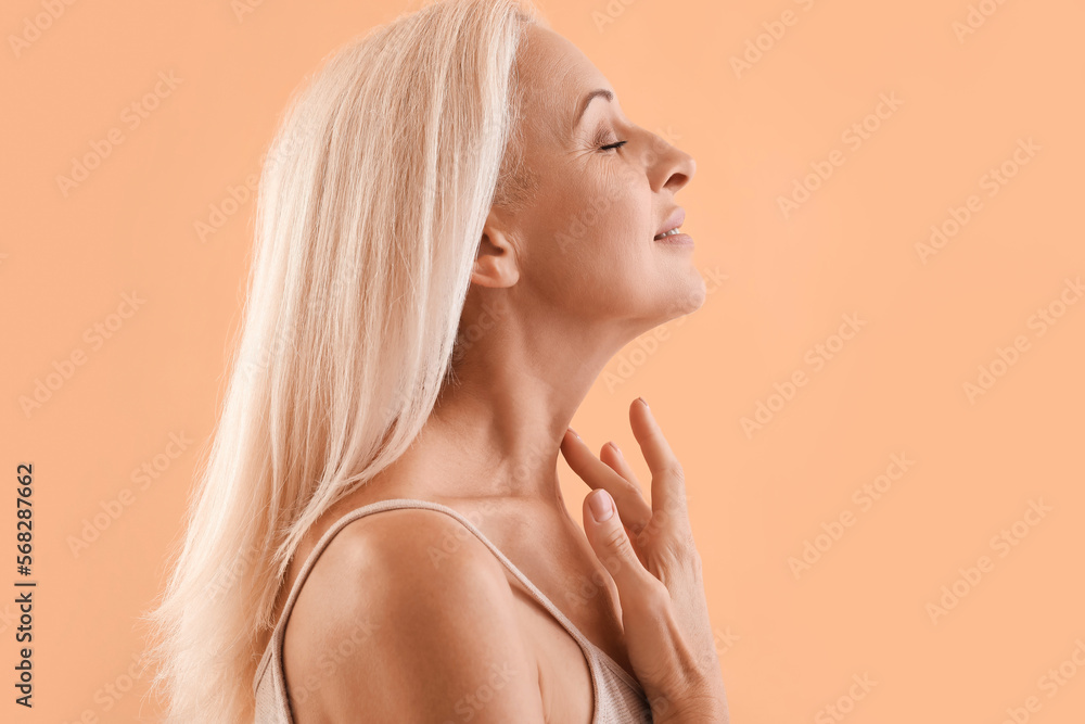 Mature blonde woman touching her neck on beige background Mature blonde woman touching her neck on beige background