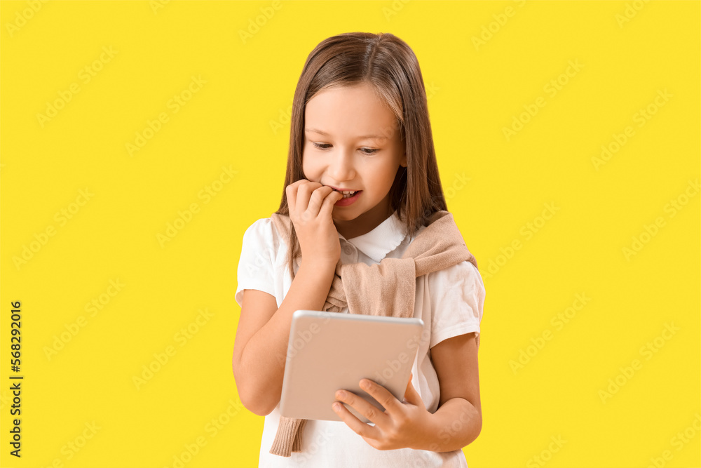 Little girl with tablet computer biting nails on yellow background Little girl with tablet computer biting nails on yellow background