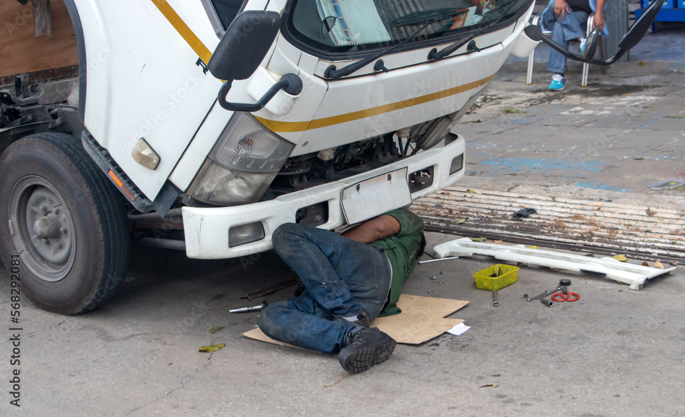 A man is repairing a truck engine on the street