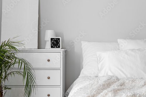 Clock with vase and painting on chest of drawers in light bedroom