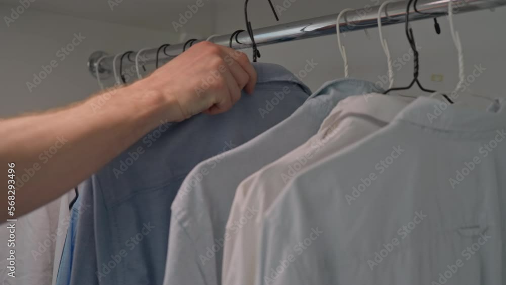 male puts hanger with blue shirt on rack with clothes at home or store male puts hanger with blue shirt on rack with clothes at home or store