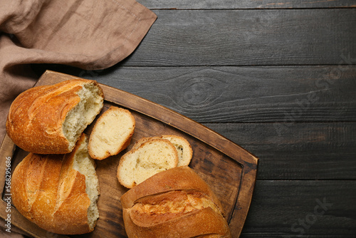Slika na platnu Cutting board with fresh sliced bread on black wooden background