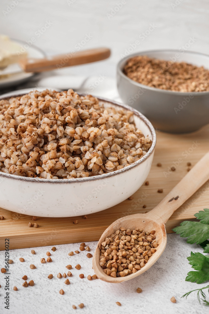 Board with bowl of tasty buckwheat porridge on white table Board with bowl of tasty buckwheat porridge on white table
