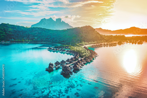 Fototapeta Luxury travel vacation aerial of overwater bungalows resort in coral reef lagoon ocean by beach