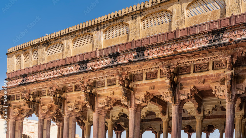 Ancient Indian architecture. The colonnade of the open hall is built of sandstone. Columns with carved capitals, arches, ornaments, patterns, lattices are visible. Blue sky. Amber Fort. Jaipur