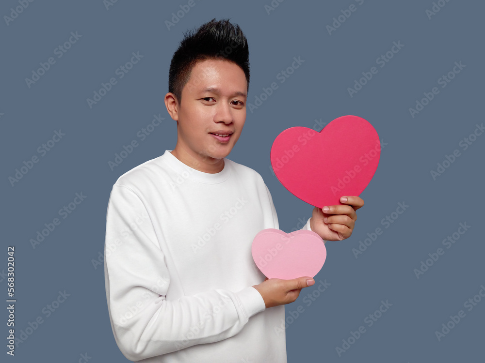 Handsome man holding and showing red and pink heart shape Handsome man holding and showing red and pink heart shape