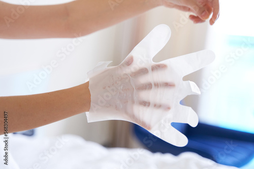 After a shower, a girl wrapped in a towel uses cosmetic gloves to moisturize the skin of her hands. Cosmetic trends for body care at home