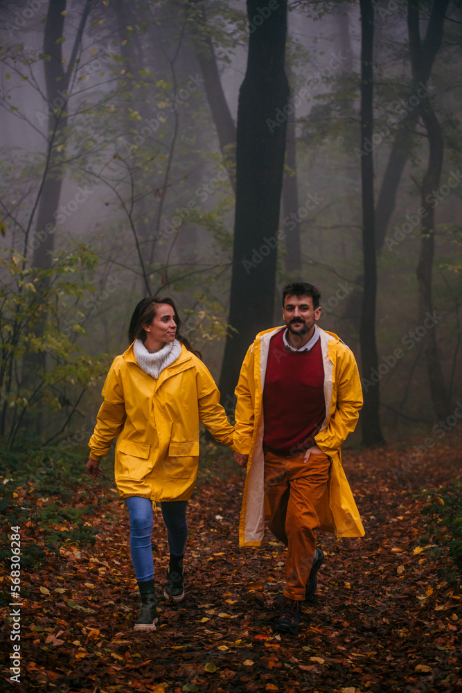 A young woman with her boyfriend in a forest, both looking around and smiling. Happy young couple walking together on a rainy day in the forest. A young woman with her boyfriend in a forest, both looking around and smiling. Happy young couple walking together on a rainy day in the forest.