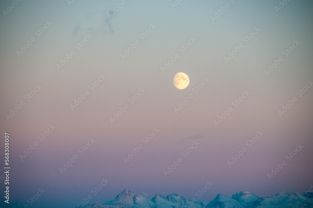 Fototapeta premium Landscape shot highlighting a near full moon over the rugged mountains of arctic Norway, near Bodo, during golden hour.